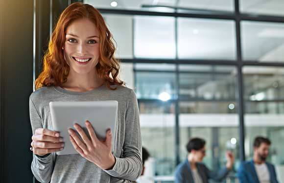 Woman smiling and holding a notepad and pencil whilst leaning against the wall