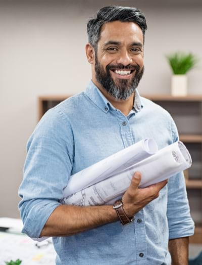 A smiling man holding blueprints, looking at the camera 