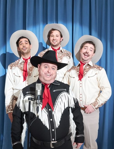 Group of singing a capella cowboys performing in front of a blue curtain.