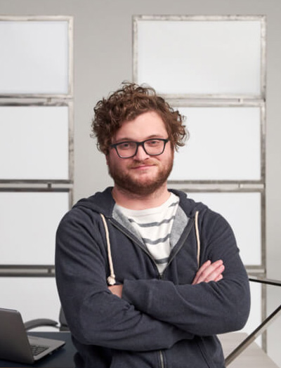 Web pro leaning on his desk with his arms crossed. There's a laptop in the background.